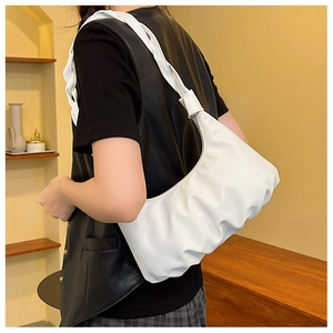 Detailed side view of white pleated cloud bag with shiny woven strap on model shoulder