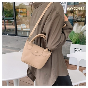 Détail du sac à main en cuir beige avec motif litchi, rabat et boucle ronde décorative