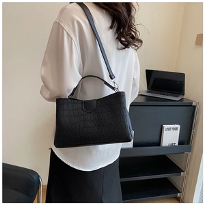 Détail d'un sac à bandoulière noir motif crocodile porté par un mannequin dans un bureau