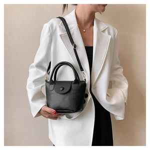 Détail d'un sac seau noir en cuir grainé porté avec un blazer blanc oversize