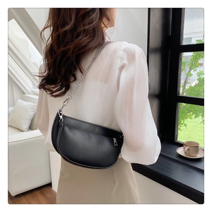 Detail of black leather half-moon bag featuring silver chain strap and front zipper pocket