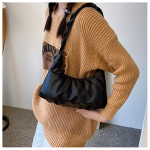 Detail of black ruched cloud bag with twisted woven strap on shoulder of a model