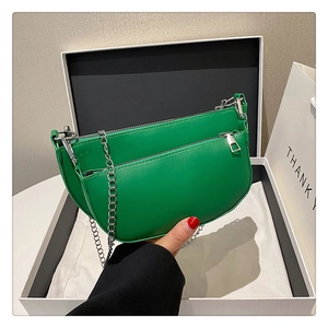Detailed view of the layered green saddle bag with a silver chain and zipper pocket