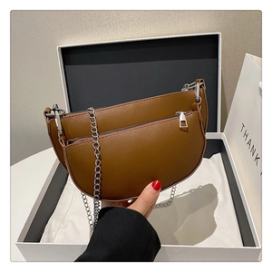 Detail of a dark brown crescent saddle bag with double layers and a sleek silver chain strap