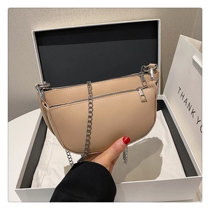 Detail of beige saddle bag featuring dual metal zippers and slim silver chain strap