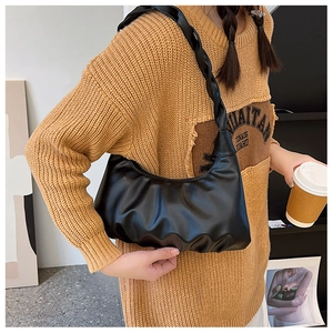 Detail of black pleated cloud bag with knotted handle shoulder strap worn by a model