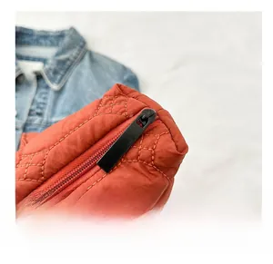 Detail of orange quilted tote bag featuring smooth metal zipper and nylon fabric