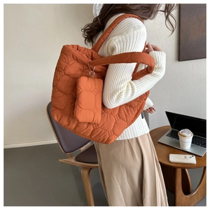 Detailed close-up of orange quilted tote bag with matching mini pouch in cafe setting
