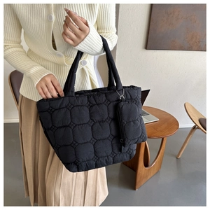 Detail of black quilted tote bag showing padded texture and matching small pendant pouch