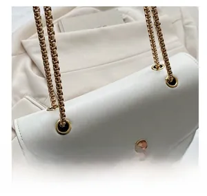 Détail macro du sac blanc avec bandoulière en chaîne dorée et fermoir rotatif en cœur