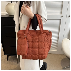 Detail of orange quilted tote bag with matching small pouch on a white coat model