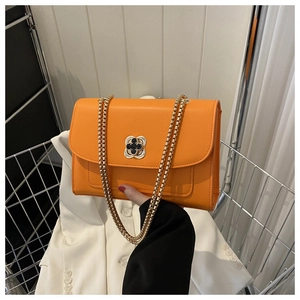 Détail du sac bandoulière orange vif avec fermoir trèfle doré et chaîne élégante