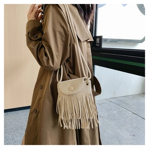 Vue détaillée du sac bandoulière crème avec de longues franges sur un trench-coat marron