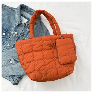 Close-up of orange quilted down tote bag with a small matching zip pouch on denim