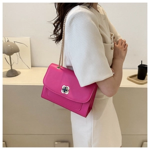 Gros plan du sac carré fuchsia avec chaîne dorée et fermoir trèfle porté par un modèle