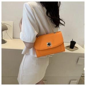 Détail d'un sac à chaîne orange vif avec fermoir trèfle doré sur une surface texturée