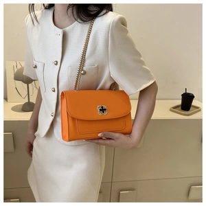 Détail d'un sac à bandoulière orange vif avec fermoir trèfle et chaîne dorée