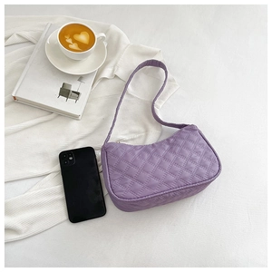 Detail view of purple quilted baguette bag styled with a coffee cup and artistic books