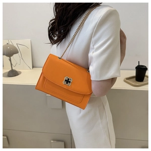 Détail du sac à bandoulière orange avec boucle trèfle dorée sur une tenue blanche chic