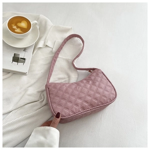 Detail of light pink quilted baguette bag with diamond stitching on white textured fabric