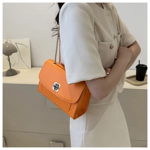 Détail du sac bandoulière orange avec fermoir trèfle doré et bandoulière chaîne
