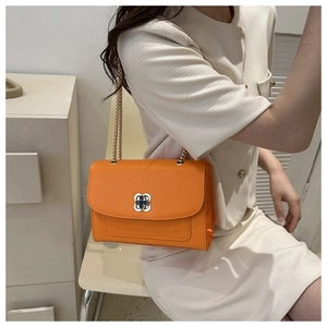 Détail du sac à rabat orange avec boucle trèfle dorée et fine bandoulière chaîne