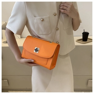 Détail d'un sac bandoulière orange vif avec fermoir rotatif fleur et bandoulière en chaîne
