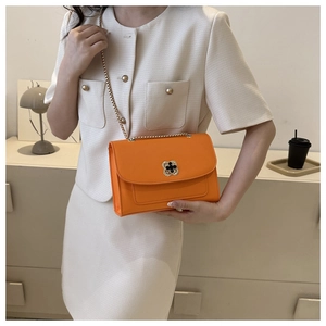 Détail du sac à bandoulière orange vif avec fermoir trèfle doré et chaîne élégante
