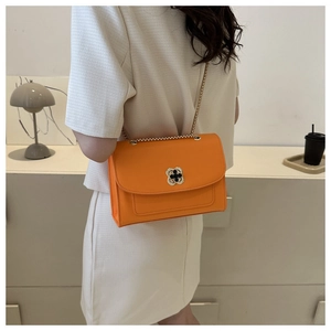 Détail du sac bandoulière orange avec boucle trèfle dorée et chaîne élégante