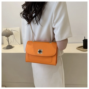 Détail d'un sac bandoulière orange vif avec fermoir trèfle en métal et bandoulière chaîne