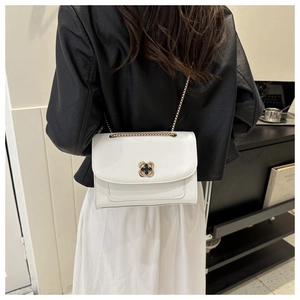 Détail d'un sac bandoulière blanc avec fermoir floral doré et bandoulière en chaîne élégante