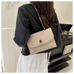 Sac bandoulière beige chic avec fermoir trèfle doré porté par un mannequin dans un bureau