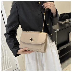 Détail du sac à chaîne beige élégant avec fermoir trèfle porté par un mannequin en veste