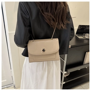 Détail du sac à bandoulière beige avec fermoir fleur doré et bandoulière chaîne portée