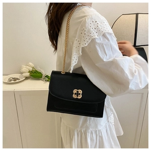 Détail du sac à bandoulière noir élégant avec boucle trèfle dorée et bandoulière chaîne sur modèle