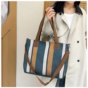 Detail of a large striped canvas tote bag with brown straps worn over a beige trench coat