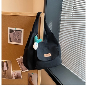 Détail du sac cabas en toile noire avec poche avant, étiquette marron et breloque en peluche