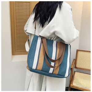 Detail view of large striped canvas tote bag with brown straps worn over the shoulder