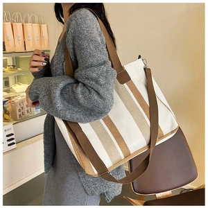 Detail view of large striped canvas tote bag with brown straps worn in a cafe setting