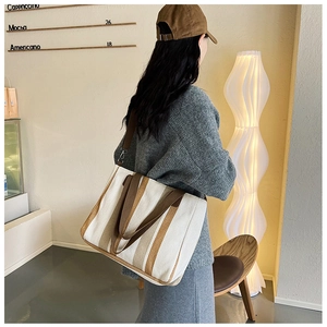 Detail shot of a large canvas striped tote bag with brown straps in a warm cafe setting