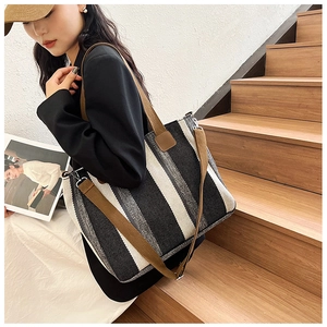Close-up of a large striped tote bag featuring brown leather handles and adjustable strap