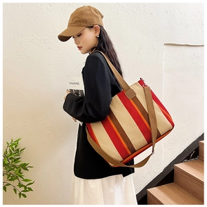 Detail of a large canvas tote bag with vertical red and brown stripes worn by a model