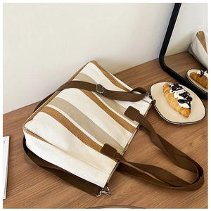 Close-up of striped canvas tote bag with adjustable shoulder strap on a wooden table