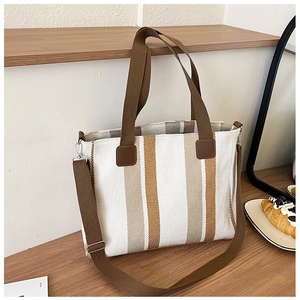 Detailed macro view of striped canvas tote bag with adjustable brown strap and metal clips