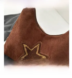Detail van een bruine suède tas met een geborduurde gele sterrenpatch en een kettingriem
