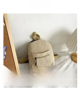 Detail shot of beige corduroy mini backpack with front zipper pocket on lace tablecloth