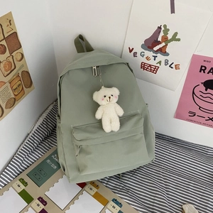 Detail view of simple nylon backpack in light green with a cute white teddy bear accessory