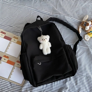 Flat lay of a black nylon backpack with a zipper pocket and a cute white bear keychain