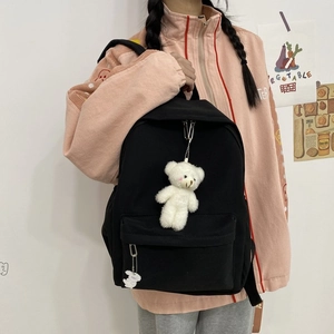 Close-up of black nylon school backpack featuring a plush bear charm and lamb pendant detail