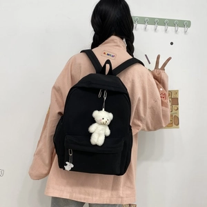 Detail of minimalist black nylon backpack featuring a cute white plush bear keychain